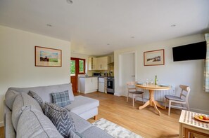 Een moderne woonkamer met een grijze bank, een eettafel met stoelen, en een keuken op de achtergrond.