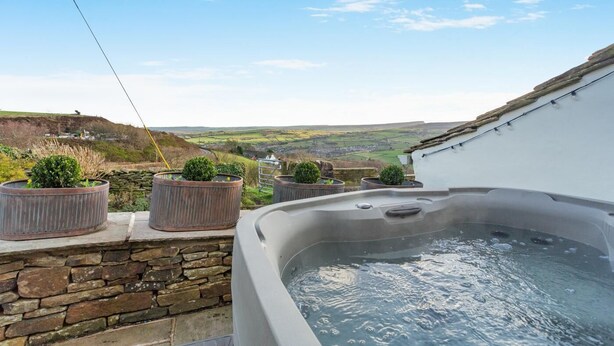 A hot tub with a stone wall and potted plants, overlooking a scenic valley. - 1 Bed in Slaithwaite (oc-c34249) (Ripponden)