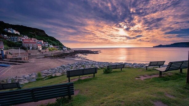 A coastal scene with a sunset, benches, a rocky beach, and houses on a hillside. - 5 Bed in Runswick (oc-wa326) (Runswick Bay)