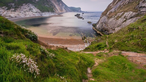Een kustlandschap met kliffen, een strand en een pad dat naar het water leidt.