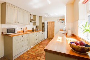A kitchen with white cabinets, a microwave, a wooden countertop, and a bowl of fruit. - 3 Bed in Yoxford (oc-bmy) (Yoxford)