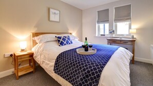 Ein ordentlich eingerichtetes Schlafzimmer mit Bett, Nachttisch mit Lampe, Schreibtisch mit Stuhl und einem Fenster mit Jalousien.