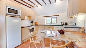 Une cuisine avec des meubles de rangement en bois, un four à micro-ondes, un réfrigérateur, une table à manger avec des chaises et une fenêtre.