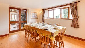 Une salle à manger avec une table en bois dressée pour six personnes, un mur en briques et une fenêtre avec des rideaux.