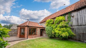 Une maison en briques avec un toit en tuiles, une grange en bois et une pelouse bien entretenue.