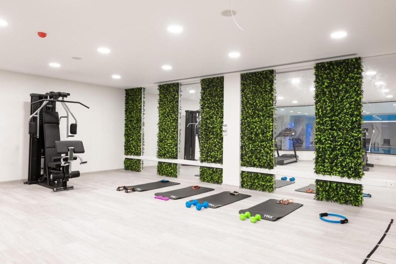 A modern gym with exercise equipment, mirrored walls, and green vertical gardens.