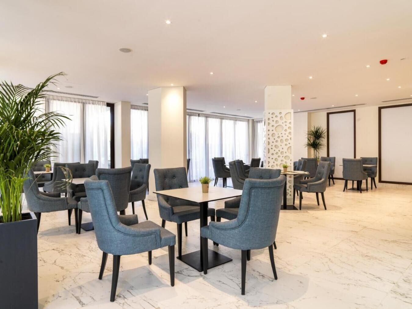 Un moderno vestíbulo de hotel con suelo de mármol, sillones tapizados grises y amplios ventanales.