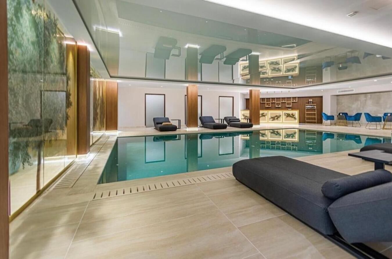 A modern indoor pool area with a glass wall, lounge chairs, and a seating area.