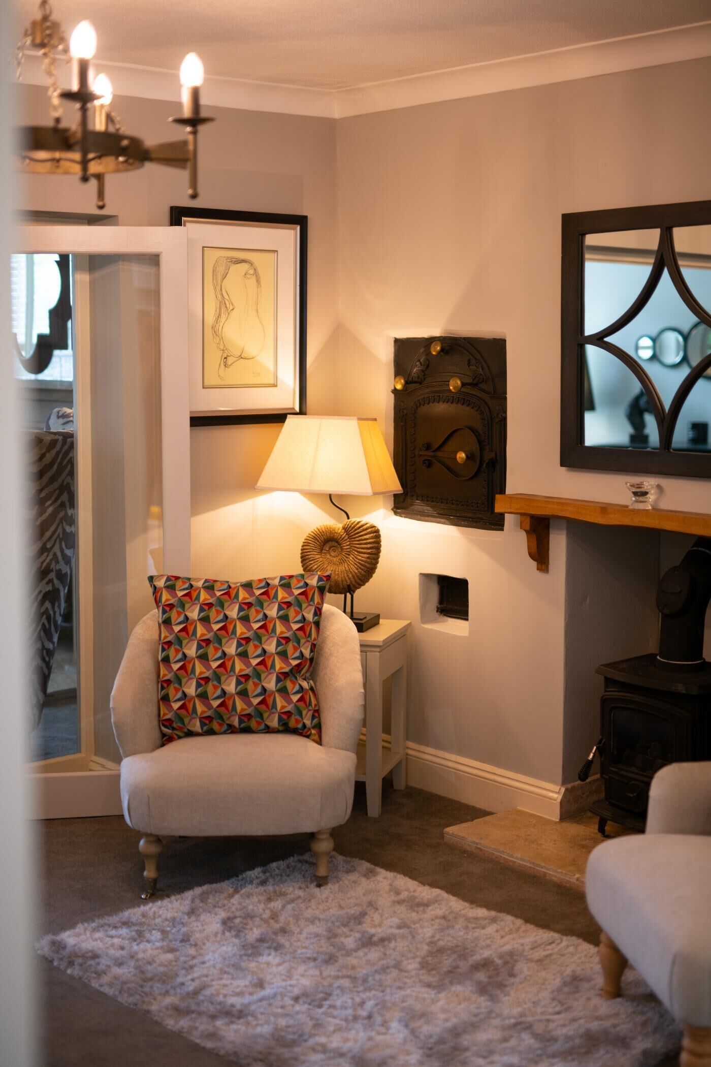 Una sala de estar acogedora con un sillón blanco, un cojín estampado, una lámpara y una chimenea.