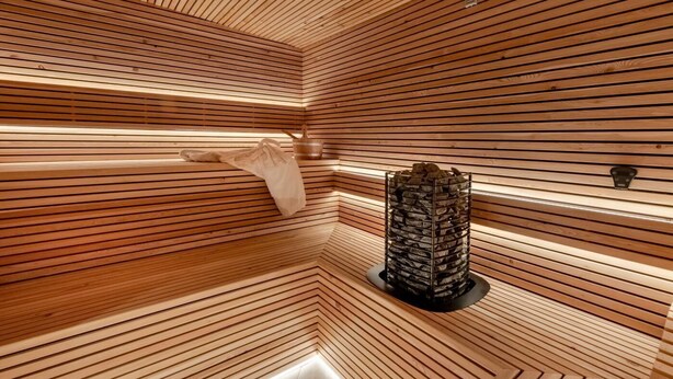 A sauna room with wooden slats on the walls and ceiling, a towel rack, and a stone heater. - 5 Bed in Scalby (oc-sa871) (Scalby)