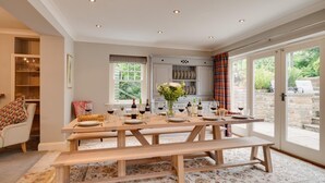 A dining area with a wooden table set for six, a bench, and a view of the garden through glass doors. - 5 Bed in Scalby (oc-sa871) (Scalby)