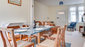 A dining area with a long table set for six, surrounded by wooden chairs with patterned cushions. A bottle of wine and several glasses are on the table. - 3 Bed in Littlestone (oc-bt009) (Littlestone)