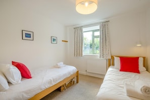 A room with two single beds, a window with curtains, a radiator, and two framed pictures on the wall.