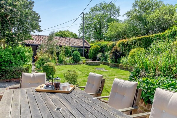Une table en bois avec quatre chaises, un plateau sur lequel se trouvent une cafetière, des tasses et une assiette de biscuits.