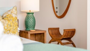 Una camera da letto con un letto, una lampada verde con decorazioni, una sedia in legno e uno specchio a parete.