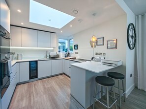 A modern kitchen with a skylight, a central island with stools, and a large clock on the wall. - 3 Bed in Constantine Bay (oc-t34218) (Constantine Bay)