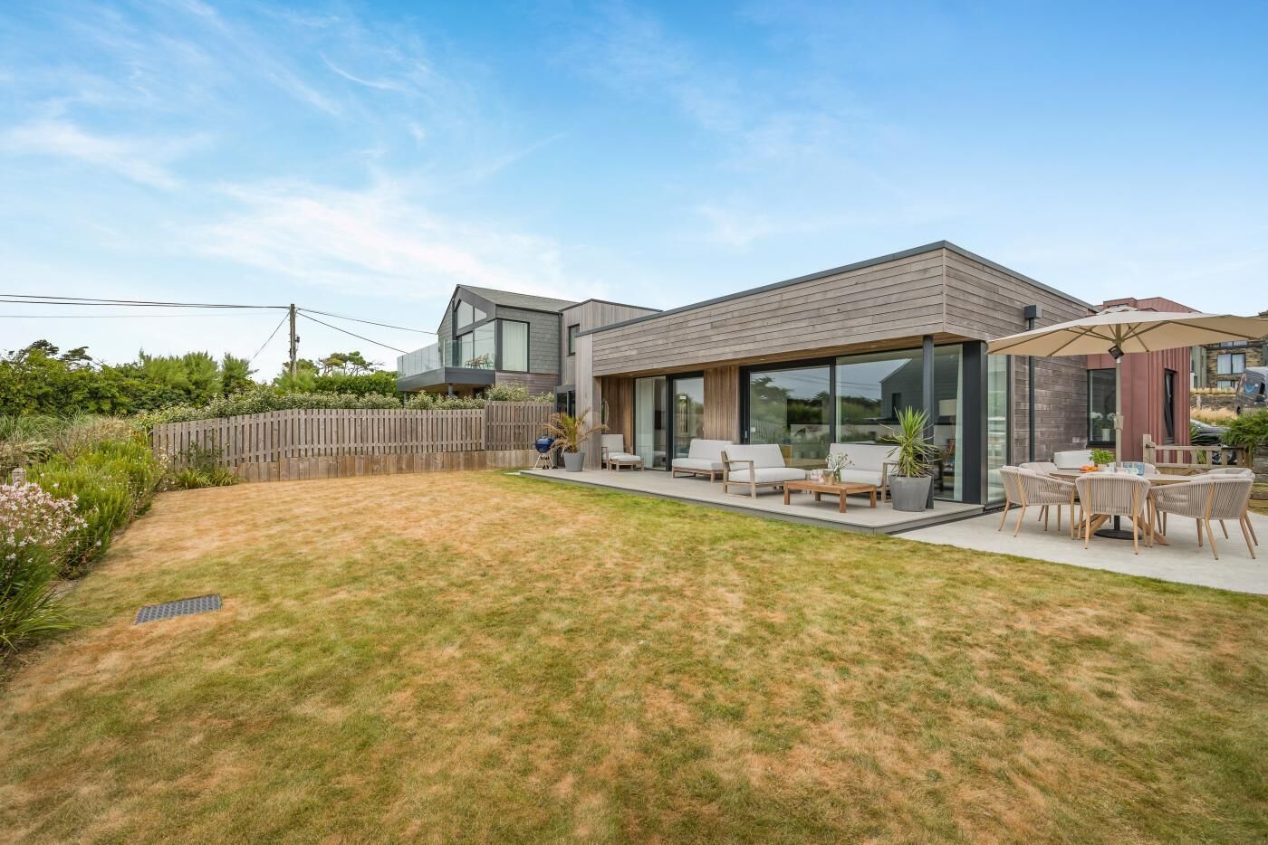 A modern house with a spacious backyard, a patio with outdoor furniture, and a large glass door leading to the interior.