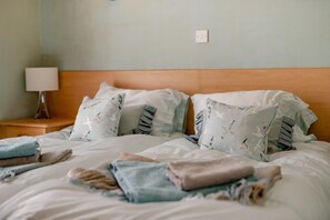 A bed with multiple pillows and folded blankets, a bedside lamp, and a wooden headboard. - 2 Bed in Scarborough (oc-s016) (Scarborough)