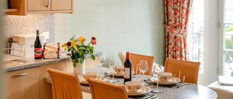A dining area with a round table set for four, wooden chairs, a vase of flowers, and a bottle of wine on the counter.