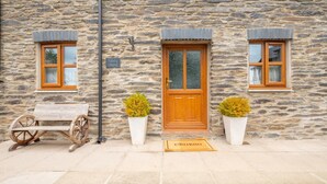 A stone building with a wooden door, two windows with shutters, a bench, and two potted plants. - 3 Bed in Aberaeron (oc-bow315) (Bethania)