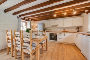 Une cuisine avec des poutres en bois, des armoires blanches, une table à manger avec des chaises et un réfrigérateur.