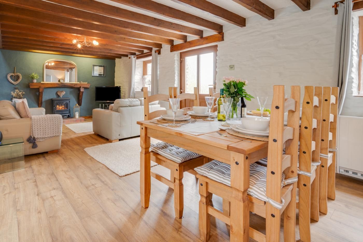 A cozy living room with a fireplace, a dining area with wooden chairs and a table set for two, and a sofa.