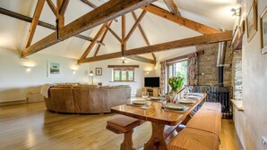 Un loft espacioso con vigas de madera a la vista, una amplia mesa de comedor de madera para seis personas, un rincón de estar acogedor y una chimenea de piedra.
