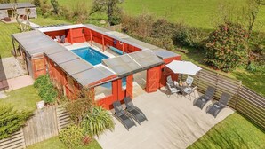 A red-roofed outdoor pool area with a glass enclosure, surrounded by a wooden deck and a grassy lawn. - 3 Bed in Nr St. Keverne (oc-tremen) (Saint Keverne)