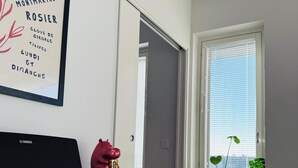 A piano, a framed poster, a red figurine, a potted plant, and a door leading to another room. - Nordic Home Bliss With Music Moments (Helsinki)