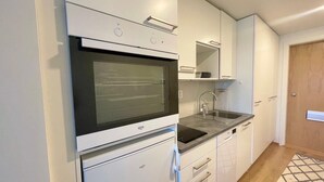 A compact kitchen with white cabinets, a built-in oven, a sink, and a wooden door. - Nordic Home Bliss With Music Moments (Helsinki)