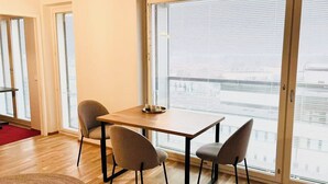 A room with a wooden table and chairs, large windows with blinds, and a view of buildings. - Nordic Home Bliss With Music Moments (Helsinki)