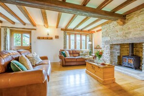 Ein gemütliches Wohnzimmer mit Ledersofas, einem Holztisch, einem Kamin aus Naturstein und freiliegenden Holzbalken.