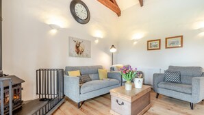Ein gemütliches Wohnzimmer mit Kamin, zwei grauen Sofas, einem Holztisch und einer Uhr an der Wand.