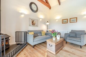 A cozy living room with a fireplace, two grey sofas, a wooden coffee table, and a clock on the wall. - 2 Bed in Wadebridge (oc-t34229) (Saint Issey)