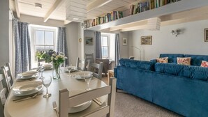 Un coin repas avec une table dressée pour quatre personnes, un canapé bleu et une bibliothèque remplie de livres.