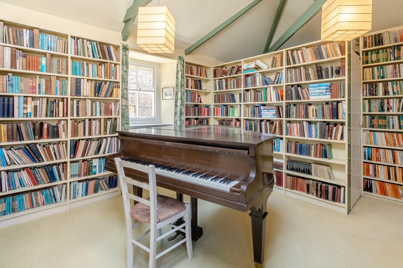 Una biblioteca amb un piano de cua, prestatges de llibres i una finestra.