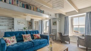 Un salon chaleureux avec un canapé bleu, une table basse en bois et une vue sur la mer grâce à de grandes fenêtres.