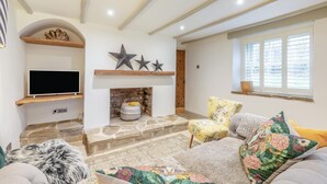 Ein Wohnzimmer mit Kamin, einem Fernseher auf einem Holzregal und einem Fenster mit Jalousien.