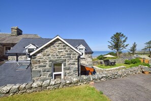 A stone house with a sloped roof, a small porch, and a view of the sea. - 2 Bed in Barmouth (oc-bow52) (Llanaber)