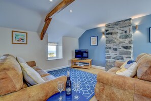 A cozy living room with a stone wall, a television, and a window with a view. - 2 Bed in Barmouth (oc-bow52) (Llanaber)