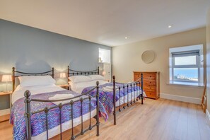 A bedroom with two beds, a wooden dresser, a round mirror, and a window with a view. - 2 Bed in Barmouth (oc-bow52) (Llanaber)