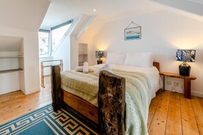 Ein Schlafzimmer mit schräg versiegelter Decke, einem Holzbettgestell, einem großen Fenster und Blick ins Freie.