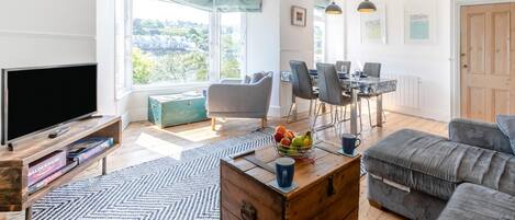 Uma sala de estar moderna com televisão, sofá, mesa de centro e espaço de jantar.