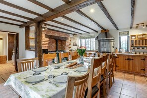 A dining area with a brick fireplace, wooden beams, and a kitchen with modern appliances.