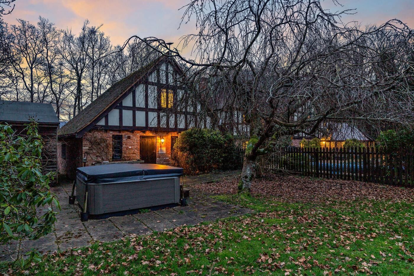 Ein traditionelles Haus im Tudor-Stil mit einer Stein-Fassade, einer Holzterrasse und einer Whirlwanne im Vordergrund.