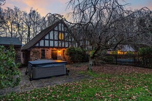 A traditional Tudor-style house with a stone facade, a wooden deck, and a hot tub in the foreground.