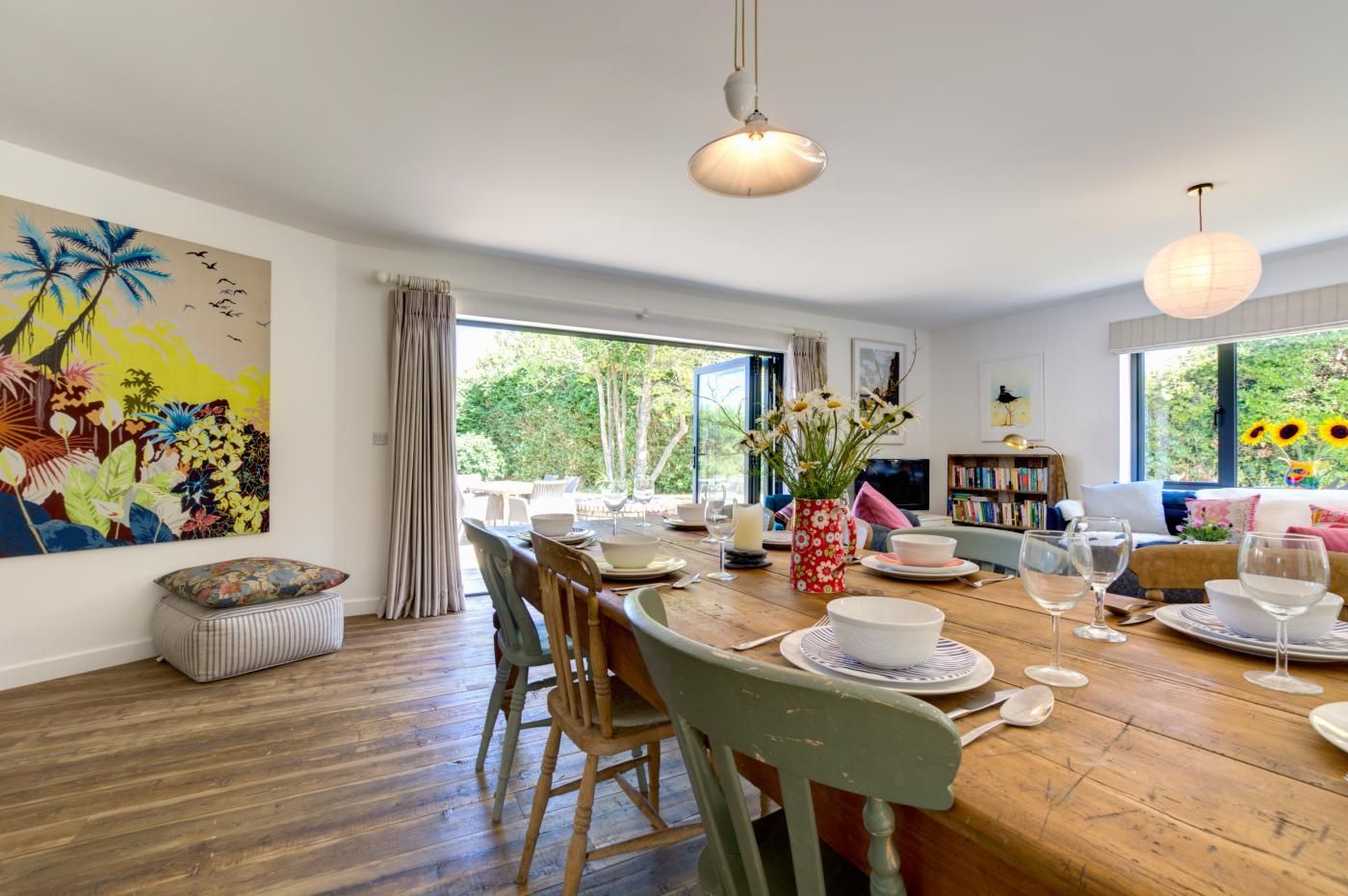 Un coin repas avec une table en bois, des chaises, un vase de fleurs et un tableau accroché au mur.