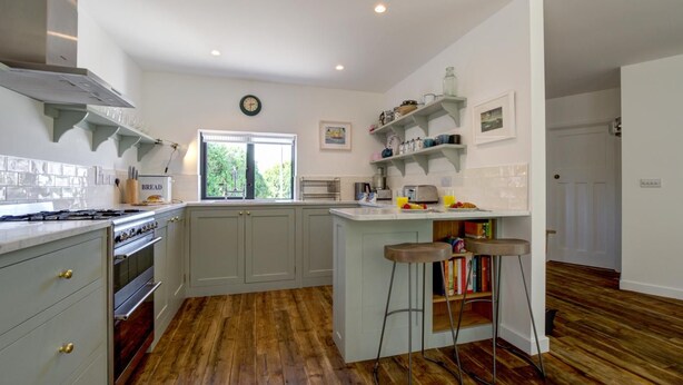 A kitchen with a large island, wooden flooring, and a window with a view of greenery. - 4 Bed in Trevone (oc-p00696) (Trevone)