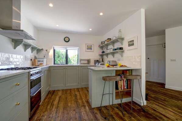 A kitchen with a large island, wooden flooring, and a window with a view of greenery. - 4 Bed in Trevone (oc-p00696) (Trevone)