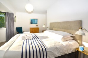 A hotel room with a large bed, a bedside table with a lamp, a dresser, and a window with curtains. - 4 Bed in Trevone (oc-p00696) (Trevone)